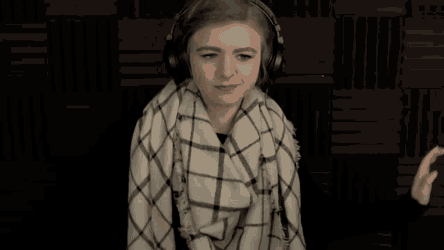 a woman wearing headphones and a plaid scarf is looking at the camera