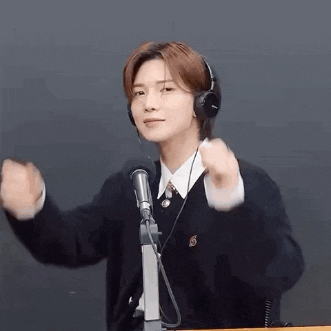 a young man wearing headphones is standing in front of a microphone and making a funny face .