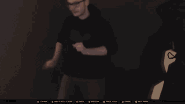 a man in a black shirt is standing in a dark room with a screen behind him with a few social media icons on it
