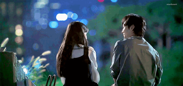 a man and a woman are standing next to each other in front of a city skyline at night .