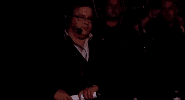 a man wearing glasses and a headset stands in front of a microphone