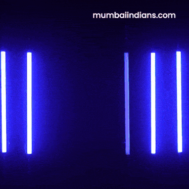 a man in a blue shirt is standing in front of a row of blue lights and the website mumbaiindians.com is below him