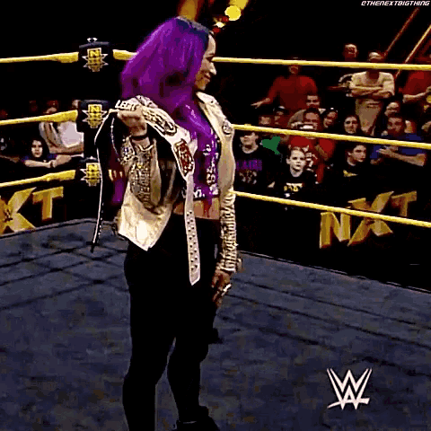 a woman with purple hair is standing in a wrestling ring holding a rope .