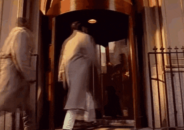 a man in a white coat is walking into a building through a revolving door .