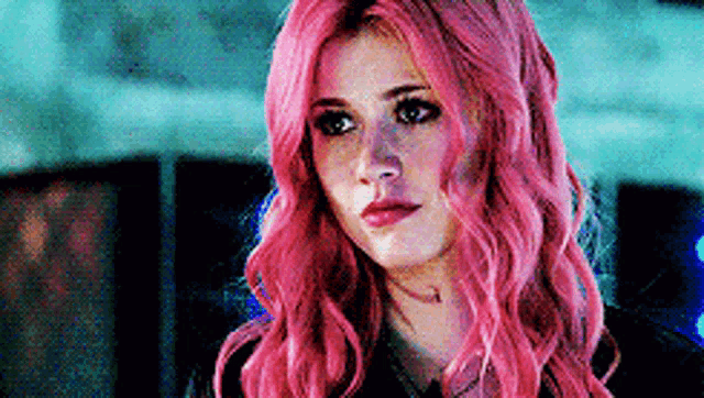 a woman with pink hair is looking at the camera .