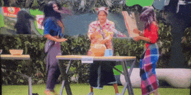 three women are standing around a table with a sign that says seconds on it