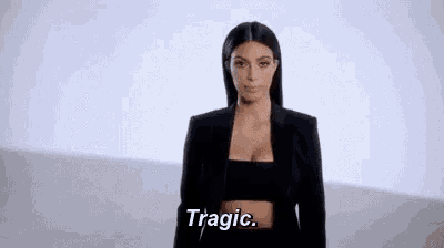 a woman in a black jacket and crop top is standing in front of a white wall and saying `` tragic '' .