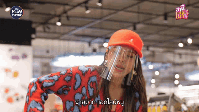 a woman wearing an orange hat and a face shield is standing in front of a sign that says play growing