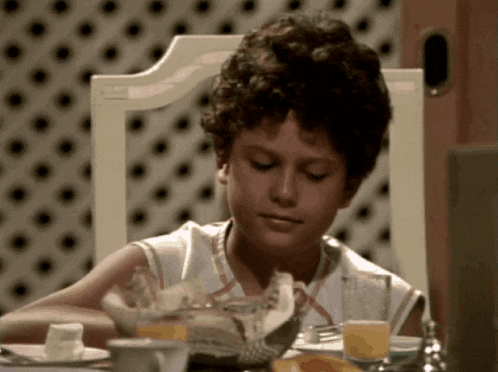 a young boy is sitting at a table with food and drinks