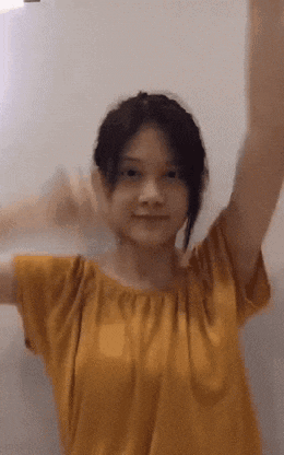 a young girl in a yellow shirt is dancing with her arms in the air