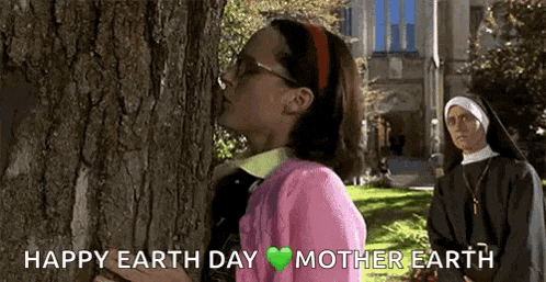 a woman in a pink sweater is hugging a tree while a nun watches .