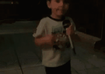 a young boy is standing in a dark room holding a bottle of water .