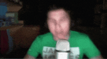 a man in a green shirt is speaking into a microphone .