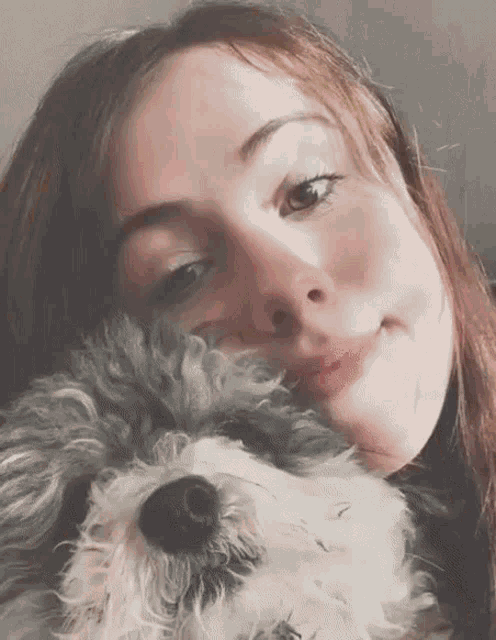 a woman is holding a small gray and white dog in her arms