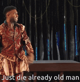 a man is standing in front of a black curtain with the words just die already old man on the bottom