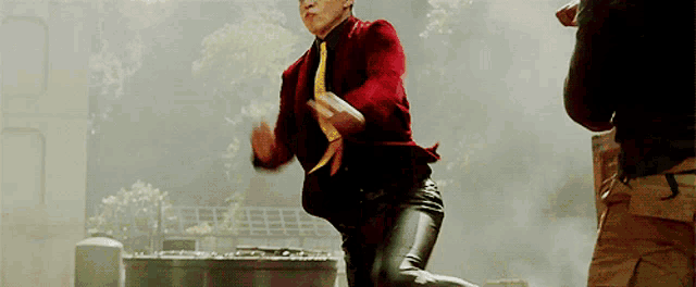 a man in a red suit and yellow tie is jumping in the air