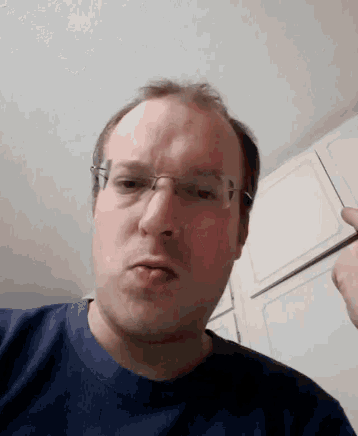 a man wearing glasses and a blue shirt makes a funny face