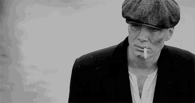a man wearing a hat is smoking a cigarette in a black and white photo .