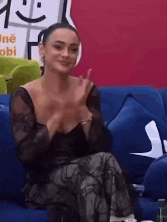 a woman in a black dress is sitting on a blue couch applauding .