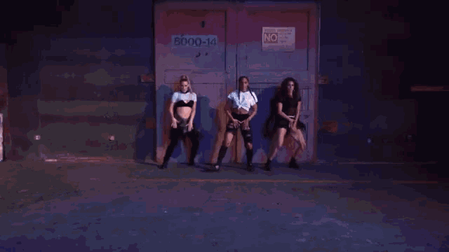 three women are dancing in front of a door that says no