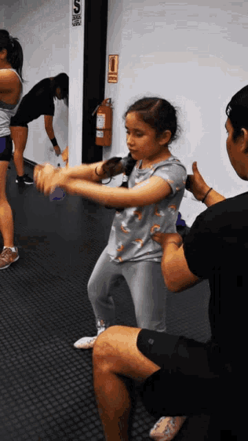 a girl in a gray shirt with a rainbow on it is being held by a man in a gym