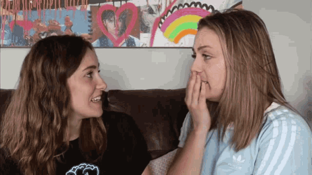 two women are sitting on a couch looking at each other and one has an adidas shirt on