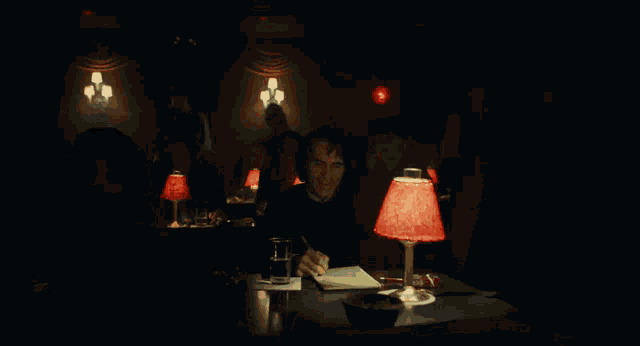 a man sits at a table in a dark room with a red lamp in front of him