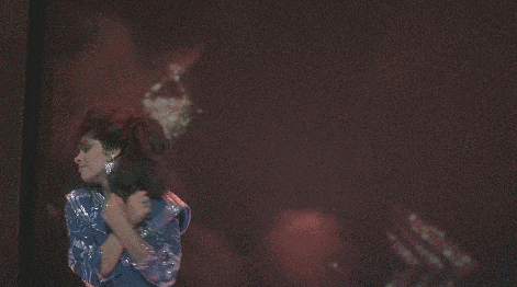 a woman in a blue dress is standing in front of a large screen with another woman 's face projected on it