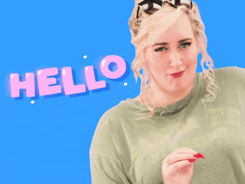 a woman wearing sunglasses and a green shirt is standing in front of a hello sign