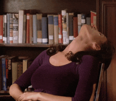 a woman in a purple shirt is sitting in front of a bookshelf with a book called allan