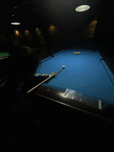 a woman is playing pool in a dark room with a blue cloth