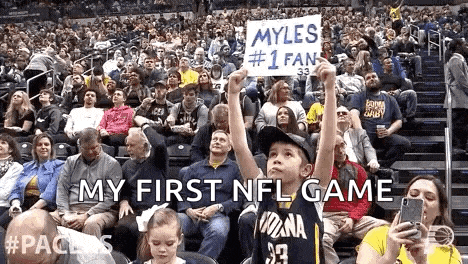 a young boy is holding a sign that says `` my first nfl game '' in front of a crowd of people .