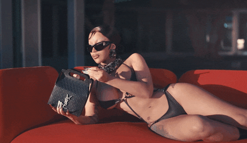 a woman wearing sunglasses is sitting on a red couch and smoking a cigarette