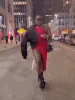 a man in a red dress is walking down a city street at night .