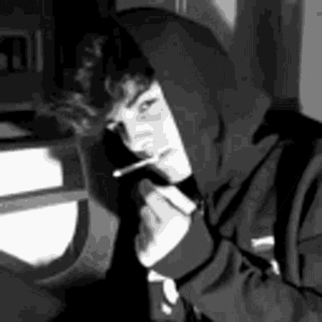 a black and white photo of a boy in a hoodie smoking a cigarette .