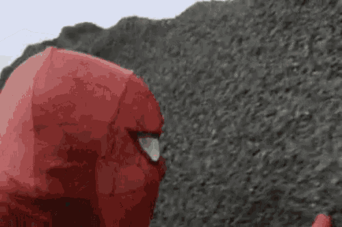 a person in a red spiderman costume is standing in front of a pile of dirt .