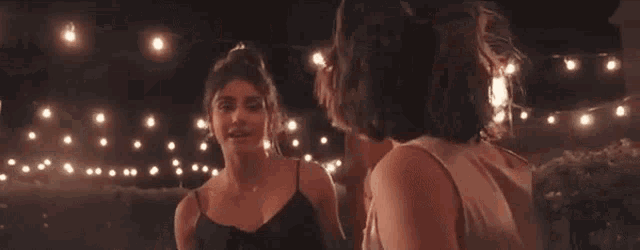 two women are standing next to each other at night and talking to each other .