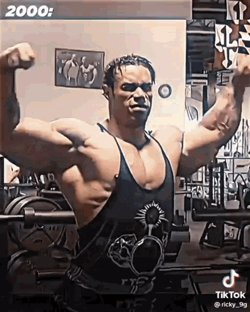 a man is flexing his muscles in a gym while wearing a tank top .
