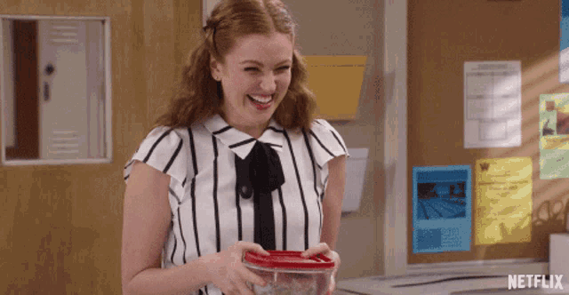 a woman in a striped shirt is holding a plastic container in front of a bulletin board that says netflix on it