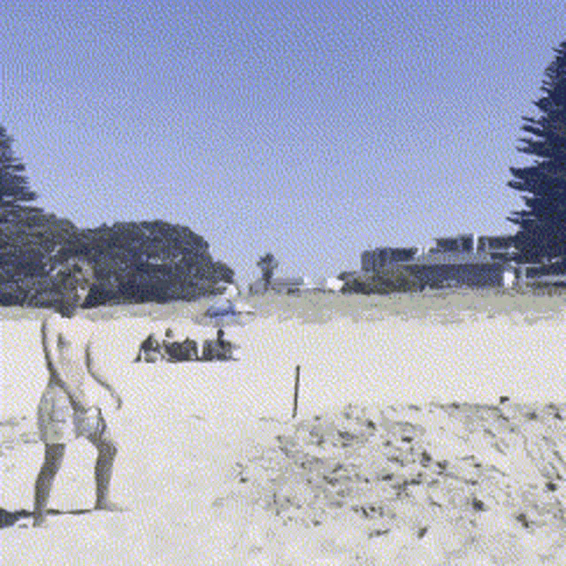 a man standing on a sandy beach with a few people sitting on the beach