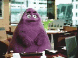 a purple monster is sitting at a desk in an office