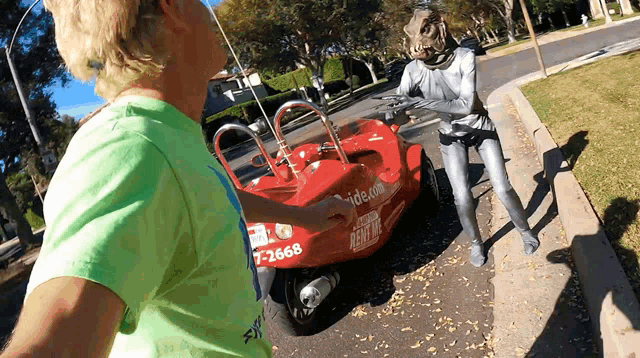 a man in a green shirt is standing next to a red car that says ride.com