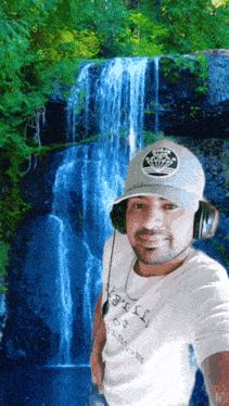 a man wearing headphones stands in front of a waterfall wearing a gray hat that says brooklyn