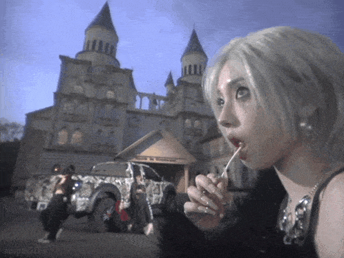 a woman with a lollipop in her mouth is standing in front of a building that says aespagifx