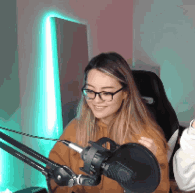 a girl wearing glasses is sitting in front of a microphone and smiling