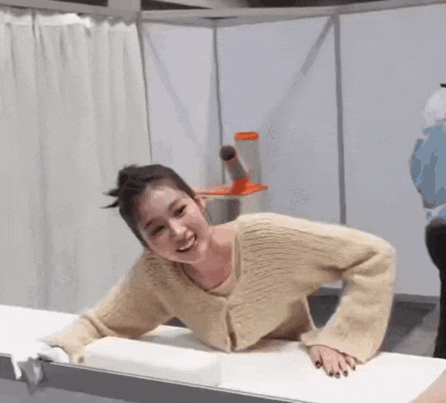 a woman in a tan sweater is laying on a white table and smiling .