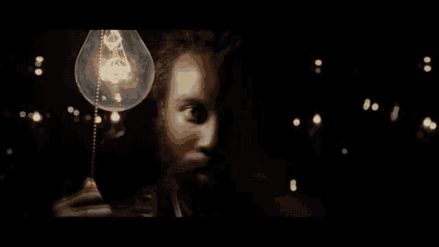 a man with a beard is holding a light bulb in front of his face in the dark .