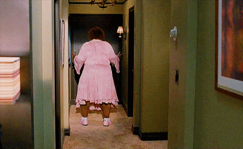 a woman in a pink robe is walking down a hallway .