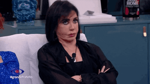 a woman sits on a couch with her arms crossed and the words grandefratello on the bottom right