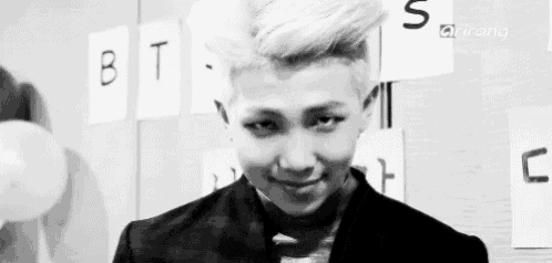a black and white photo of a young man with a mohawk and the word bts on the wall behind him .